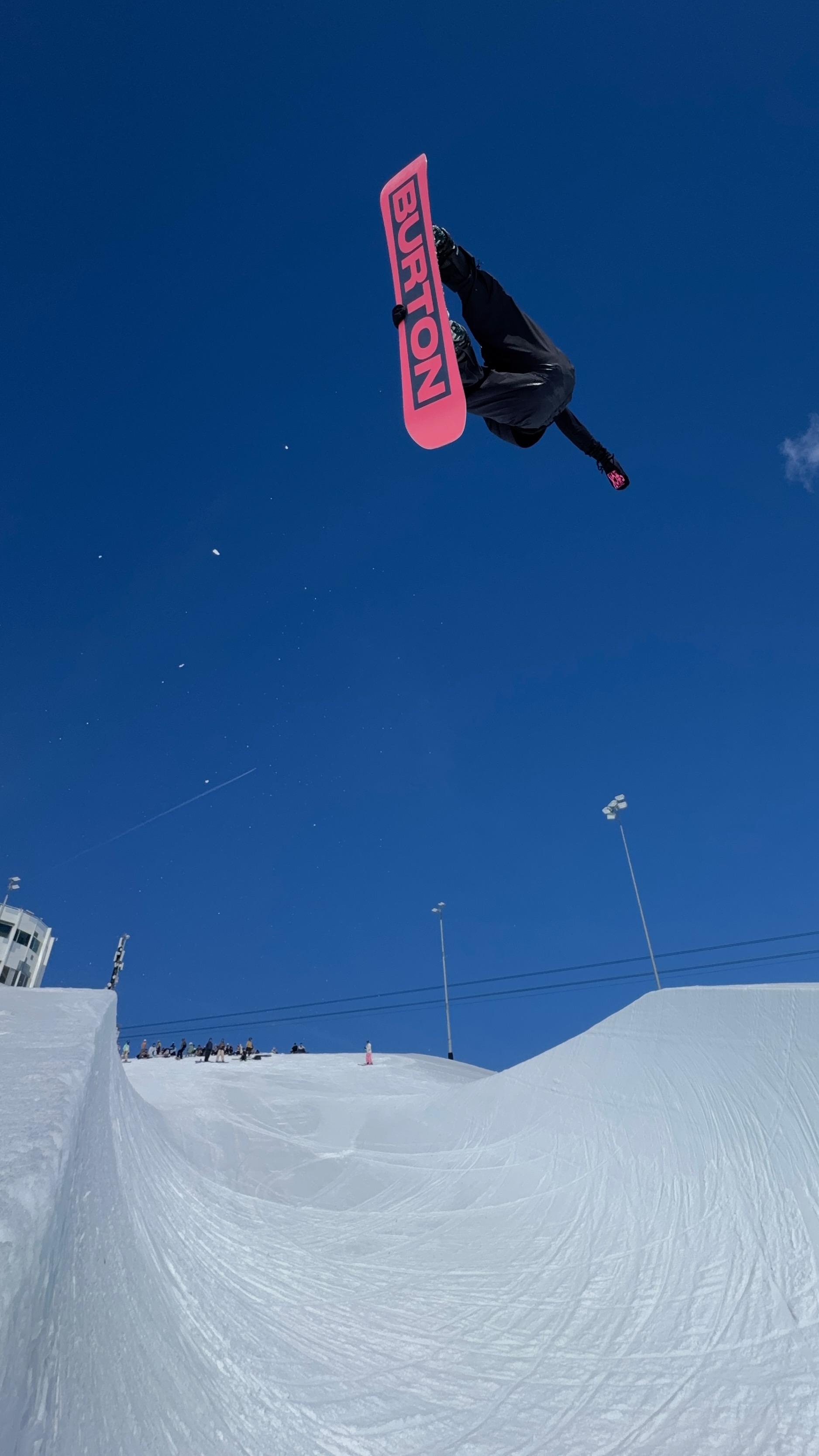 Jonas Hasler performing an inverted snowboard aerial against a blue sky