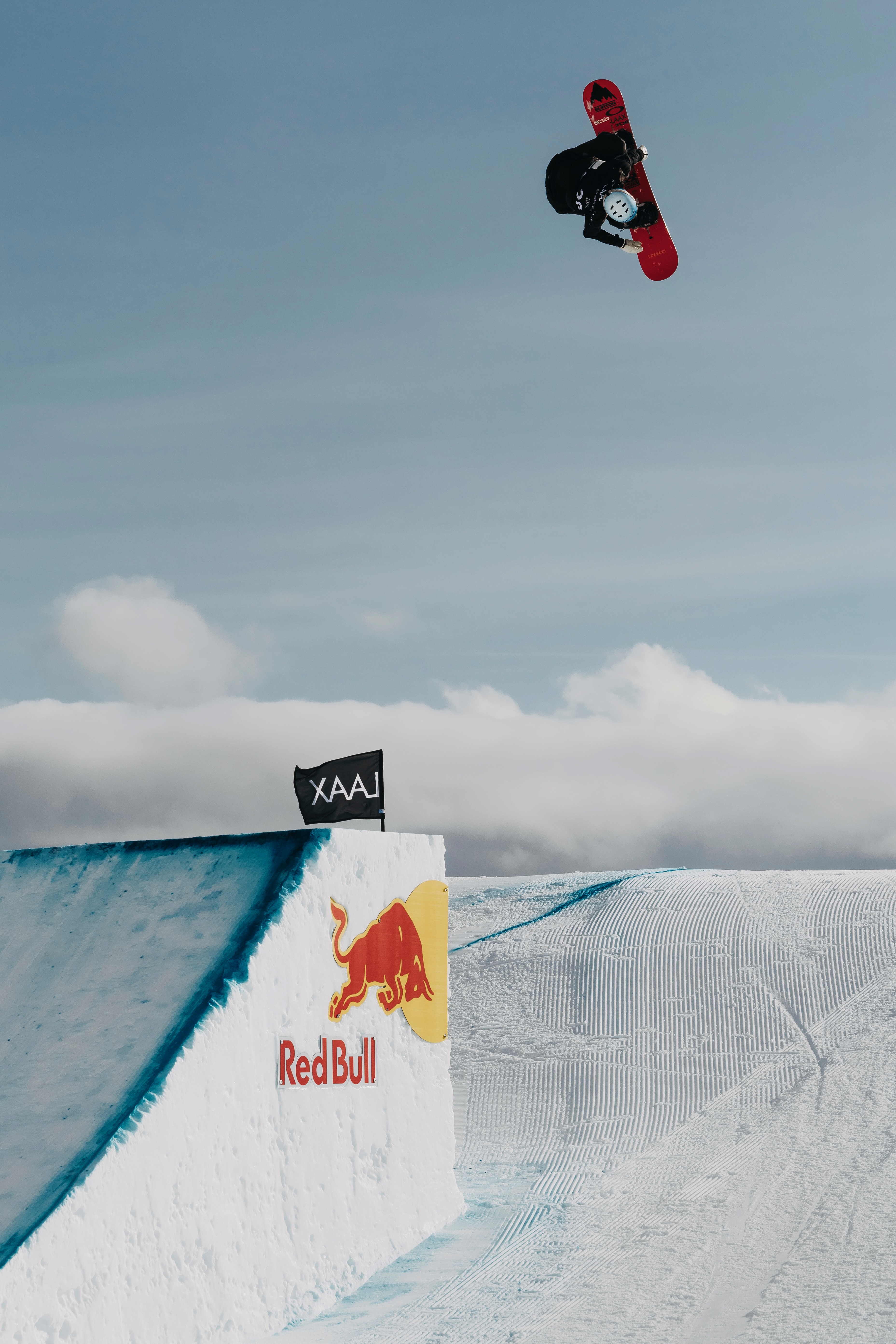 Jonas Hasler rotating above the snowboard halfpipe with his red Burton board